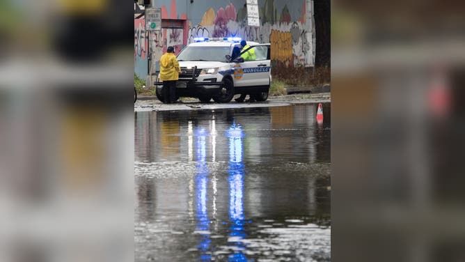 Police officers from the Honolulu Police Department block a flooded street near the Hawaii Convention Center in Honolulu, Hawaii, on August 16, 2026. Hurricane Lala was pulling away from Hawaii's Big Island early Sunday, as heavy rain and strong winds struck the US Pacific state and officials warned of potentially dangerous flooding. The heavy rain and flood risk will then spread westward across the island chain on Sunday, according to the NHC.