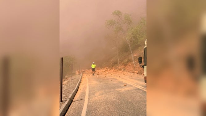 A worker in a hard hat stands in the dust near the rockfall in Zion National Park on Aug. 24, 2026.