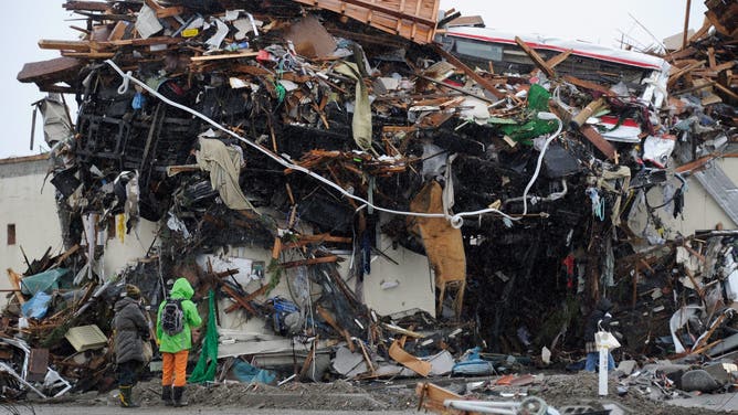 Local residents look at a mountain of debris left by the March 11 tsunami and earthquake in Natori in Miyagi Prefecture on March 16, 2011.