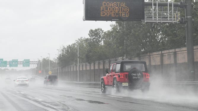 A car passes under a sign warning of expected coastal flooding during a major nor'easter near Atlantic City, New Jersey, on September 26, 2026. Heavy rain and strong winds battered the northeastern United States as an unusually powerful autumn storm intensified, forcing the cancelation of hundreds of flights and leaving tens of thousands of people without power. New York, Boston and Philadelphia were all in the firing line of the "Nor'easter" -- so labeled for its northeasterly winds -- as authorities warned of potential major flooding and road closures.
