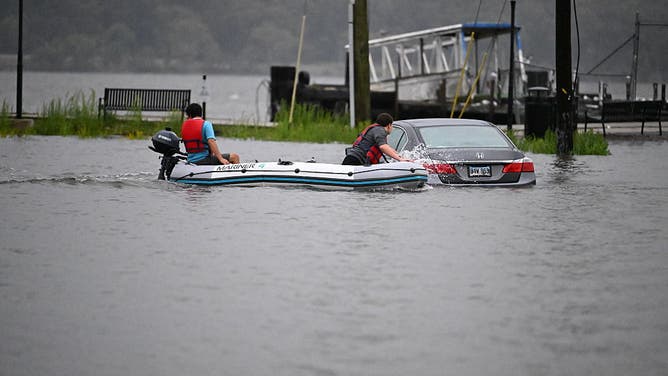 EDGEWATER, NEW JERSEY, USA - SEPTEMBER 26: Two people on a boat look closely at a vehicle submerged in floodwaters in the parking lot along the Hudson River during a nor'easter storm in Edgewater, New Jersey, United States, on September 26, 2026.