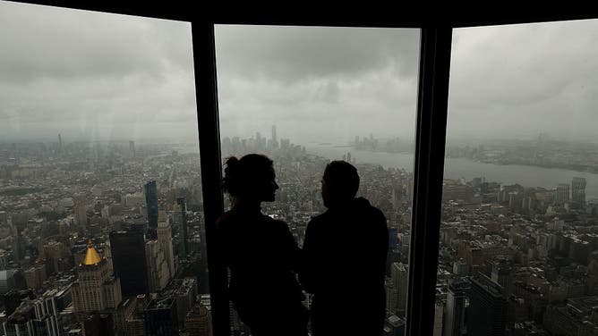 NEW YORK, NY - SEPTEMBER 26: People look out the window of the 102nd-floor observation deck of the Empire State Building as a nor'easter passes over lower Manhattan and One World Trade Center on September 26, 2026, in New York City.