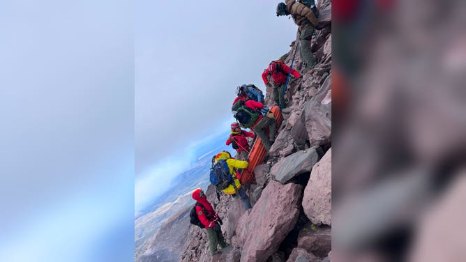 The rescuers making an almost vertical descent with the stretcher that carries the injured man.