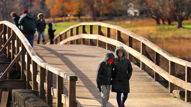 CONCORD, MA - NOVEMBER 8: Pedestrians are bundled up as they walk across the Old North Bridge that spans the Concord River in Concord, NH on a cold fall afternoon on Nov. 8, 2019.