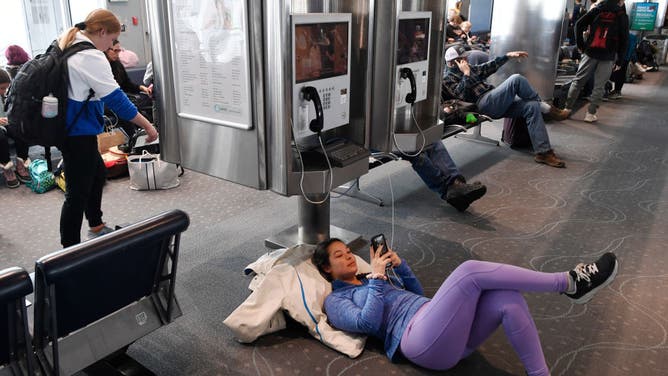 DENVER, CO - NOVEMBER 26: University of Colorado Colorado Springs student Rachel Ottoson, right, checks her phone while charging it during her fourth flight delay trying to get to Minnesota for Thanksgiving at Denver International Airport November 26, 2019. Many flights were canceled or delayed due to a heavy snowstorm in the area.