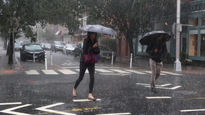 HOBOKEN, NJ - SEPTEMBER 29: People walk down the middle of a street during a heavy rain storm on September 29, 2023, in Hoboken, New Jersey. Much of the Northeast is experiencing severe flooding after heavy rains swept through the area this morning.