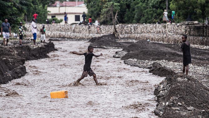TOPSHOT - Children walk through a flooded street in the aftermath of Hurricane Melissa, in Petit-Goave, about 68 km (42 miles) southwest of Port-au-Prince, on October 31, 2025.